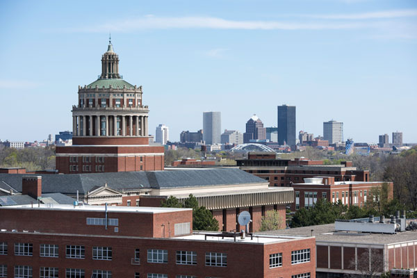 View of the University of Rochester campus skyline from a rooftop, showcasing city buildings against a clear sky.