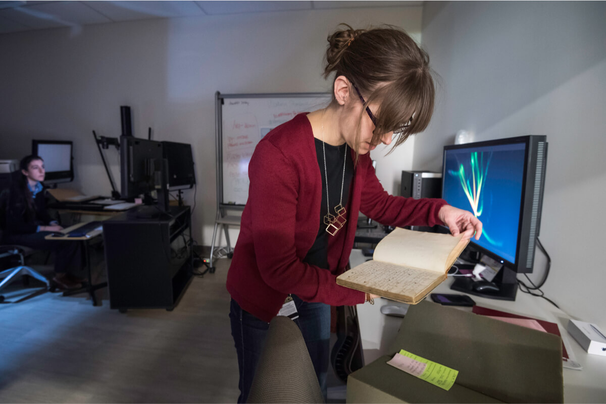 A woman examines an open book on a desk in the University of Rochester library lab.
