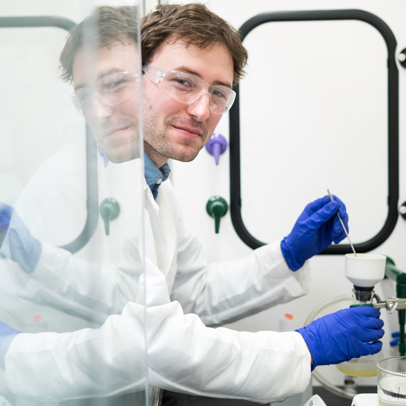 A researcher in a lab coat and gloves conducts experiments in the University of Rochester research lab.