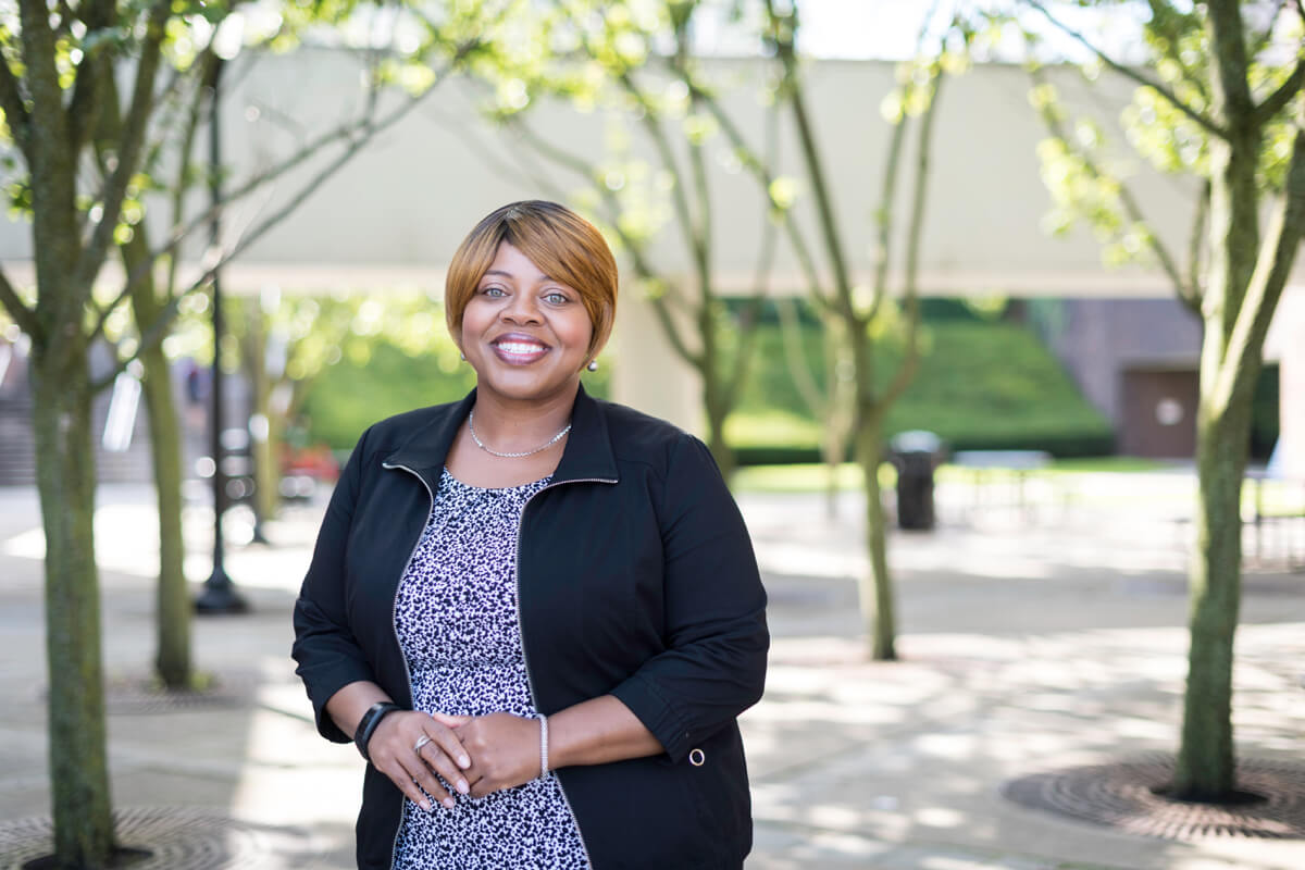 Dawn Bruner, a staff member at the University of Rochester, poses on campus with trees in the background.