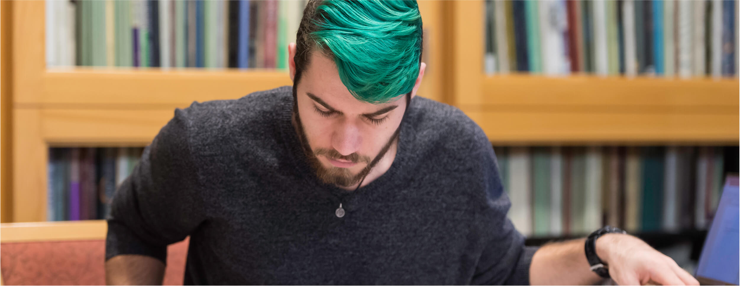A University of Rochester student with green hair sits at a table, reviewing papers and studying intently.