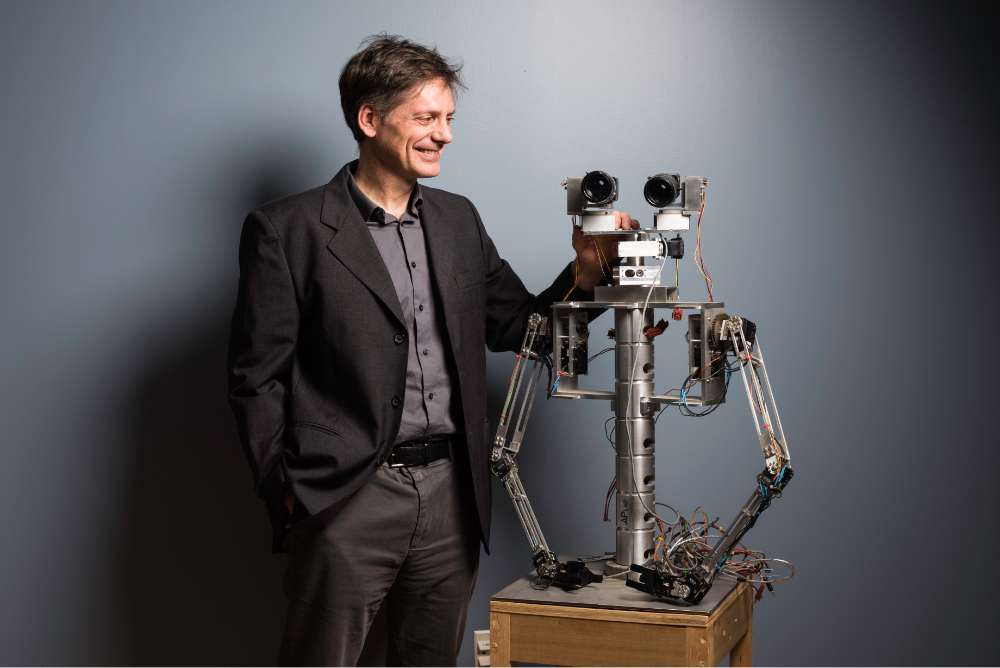 Faculty robotics researcher standing next to robot head and upper torso at University of Rochester.