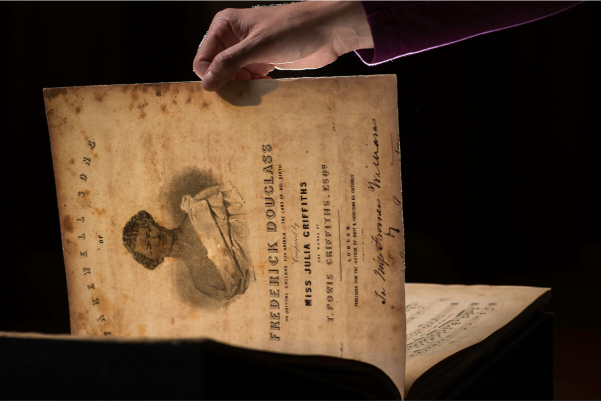 A person holds a book with an old paper on it in the University of Rochester library lab.