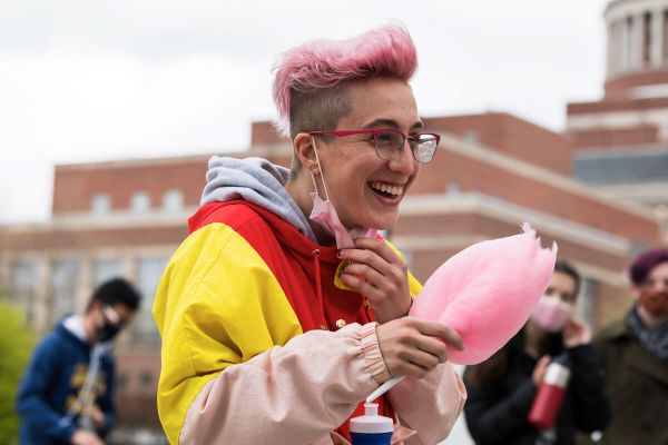 A University of Rochester student with pink hair and glasses holds a fluffy cotton candy treat, smiling at the camera.