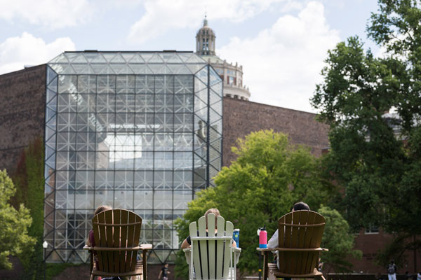 Two people relax in lawn chairs on the University of Rochester campus, with a building visible in the background.