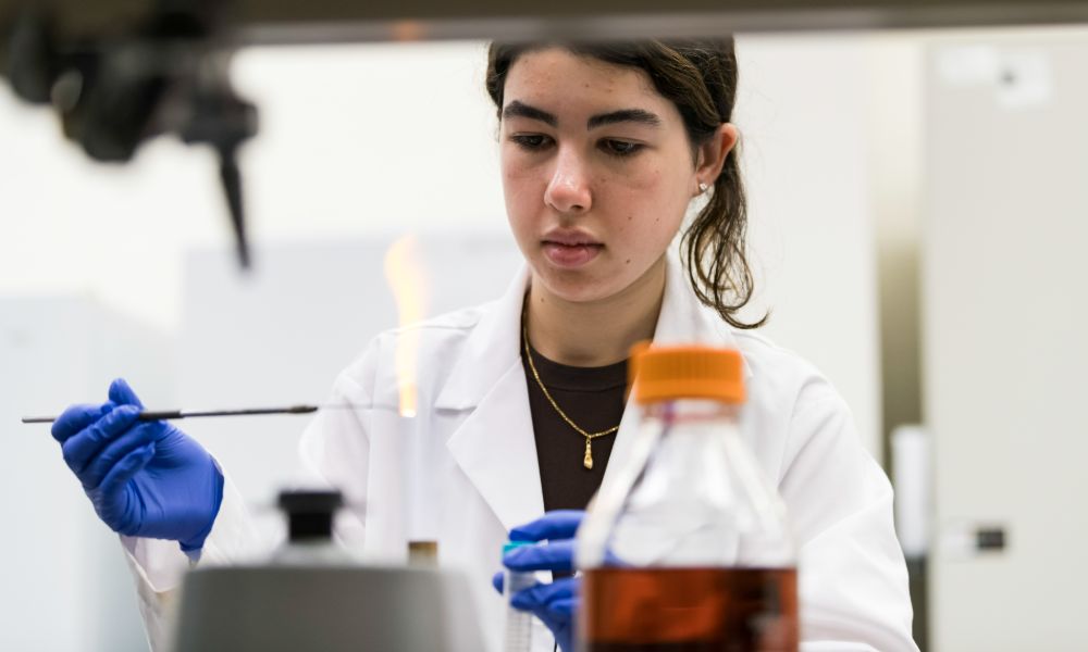 A female scientist in a lab coat conducts research in a laboratory at the University of Rochester.