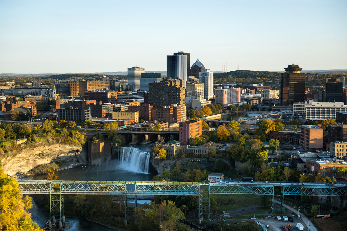A panoramic view of Rochester from a hilltop, showcasing the skyline and urban landscape, with the University of Rochester nearby.