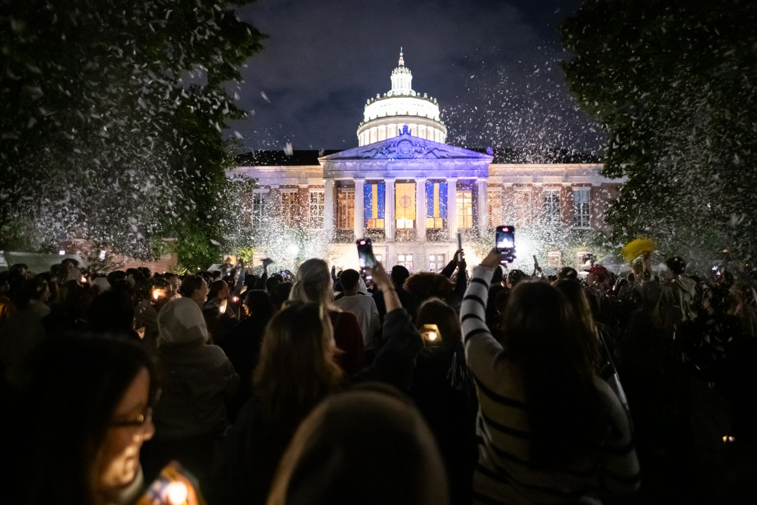 A group of individuals gathers outside the University of Rochester's capitol building, lighting candles in remembrance.