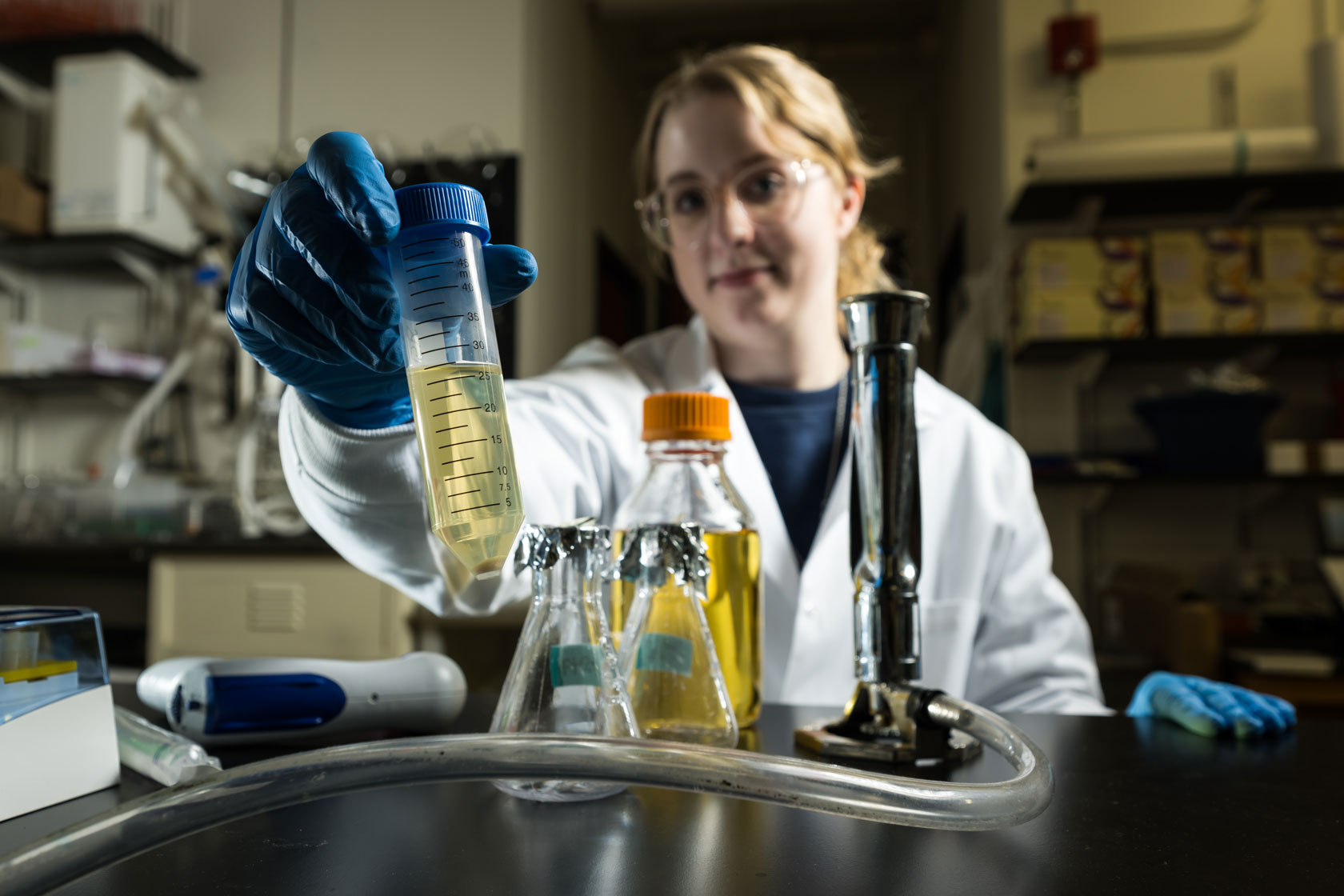 A University of Rochester student in a lab coat holds a test tube, focused on her experiment in a laboratory setting.