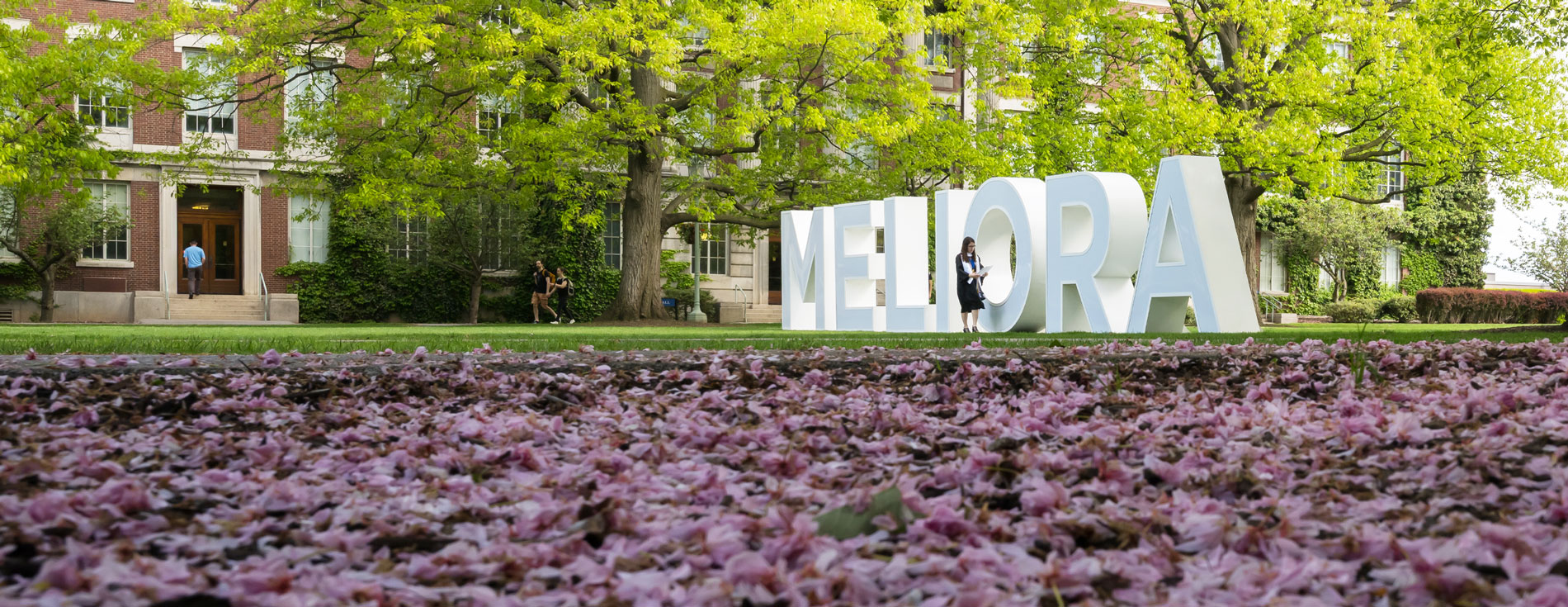  University of Rochester student poses in front of MELIORA letter installation during Commencement Weekend.