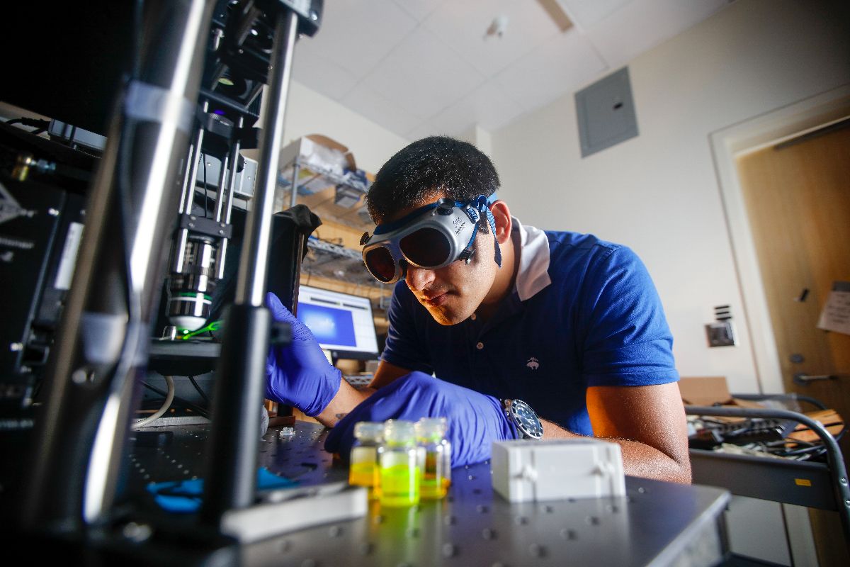 A man in a blue shirt and goggles operates a machine, showcasing hands-on work by URochester students.