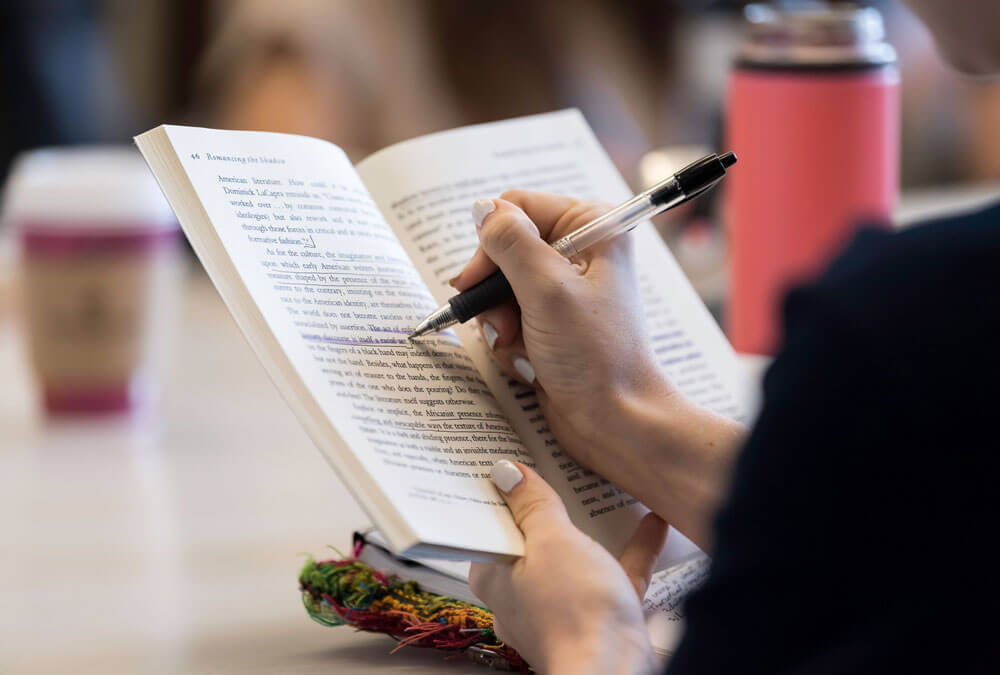A University of Rochester student reading a book while seated at a table, focused on the text.