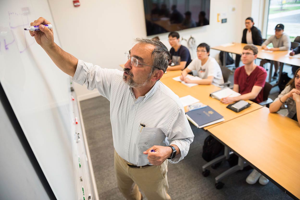 Professor writing on a whiteboard at the front of a classroom at the University of Rochester.