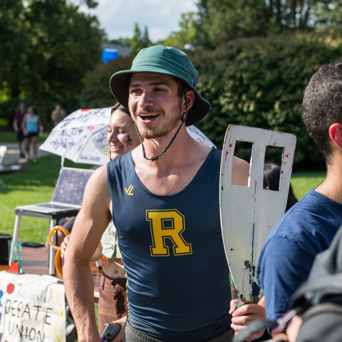 University of Rochester athlete wearing a bucket hat and University branded tank top holds an oar