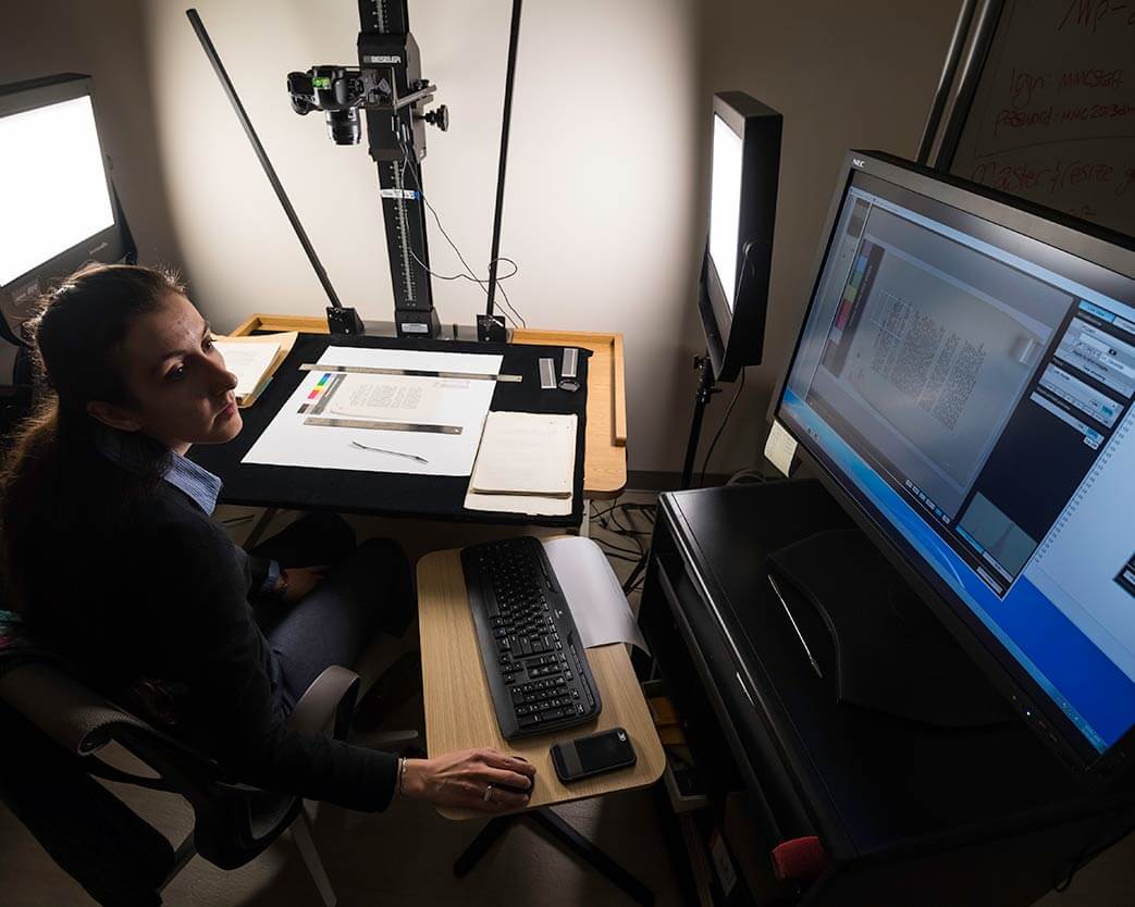 Researcher working on digitizing printed materials with a computer display in the background