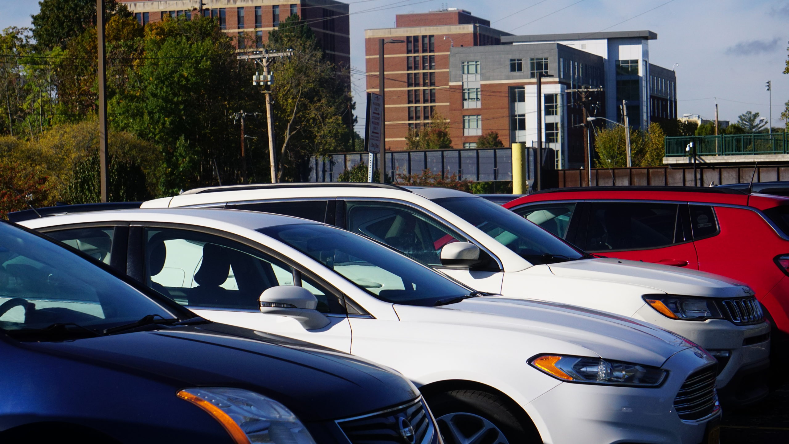 Vehicles parked in University of Rochester lot with brick buildings in background