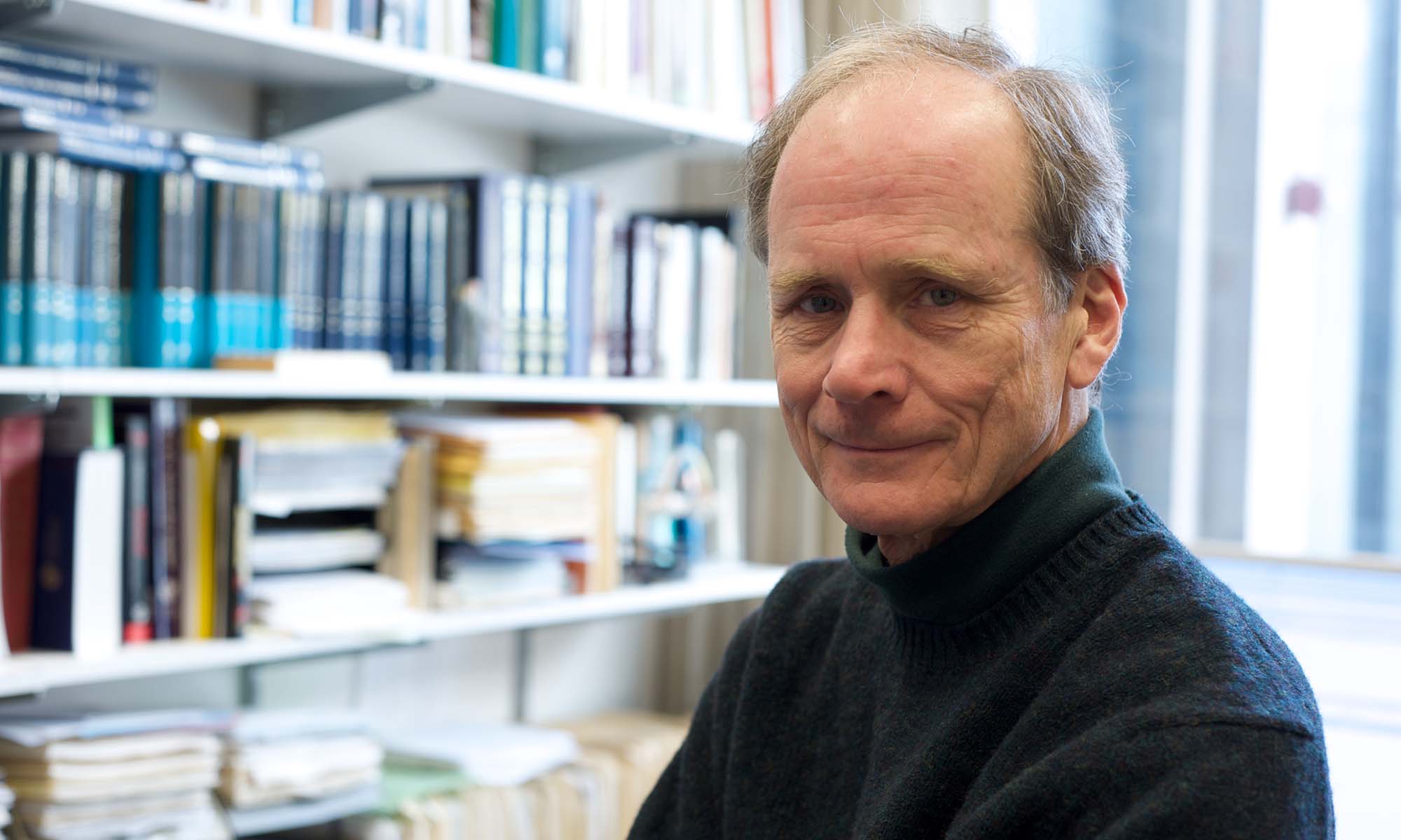URochester psychologist Edward Deci smiles and looks at the camera with his office bookshelves out of focus in the background.