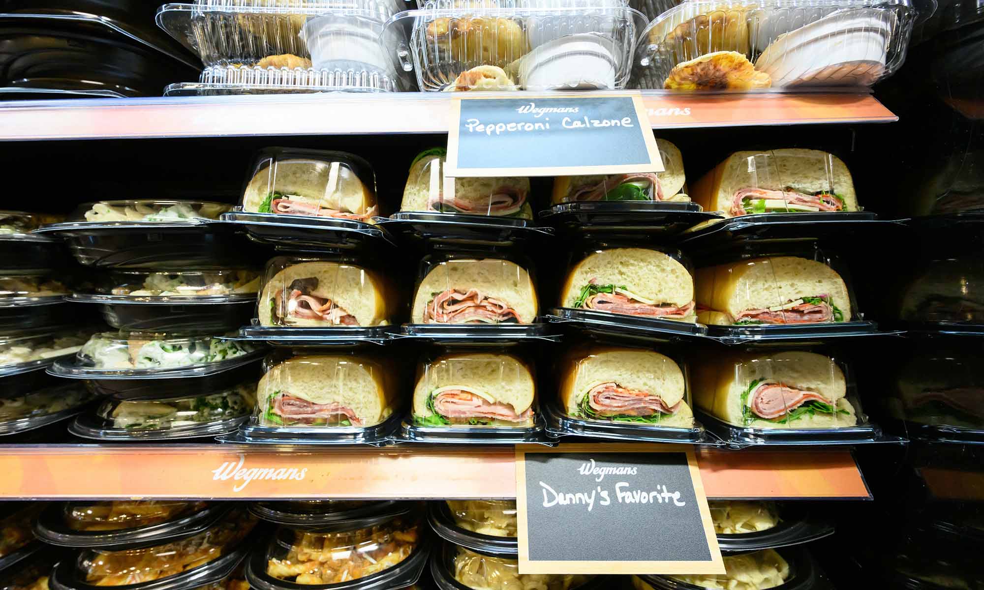 Close up of Wegmans sandwiches, prepared meals, and pepperoni calzones on display at Hillside Market at the University of Rochester.
