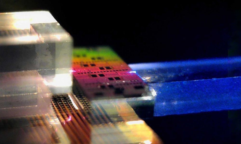Close up of a rainbow-hued photonic chip coupled to a clear and metallic nonlinear crystal and fiber array unit.