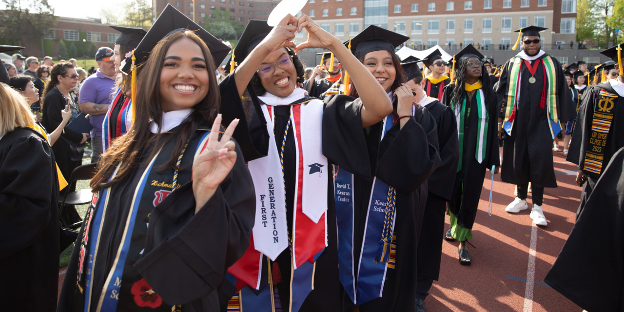 Students in caps and gowns smiling and posing at commencement