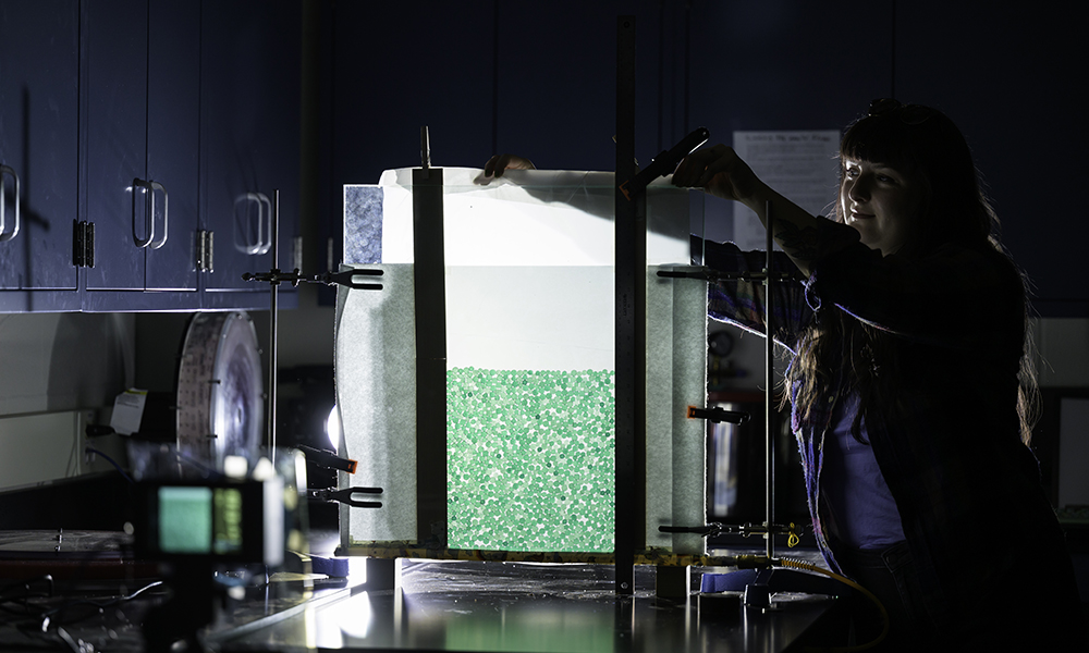A person holding a sheet displaying a pattern up to a light source in a lab setting.