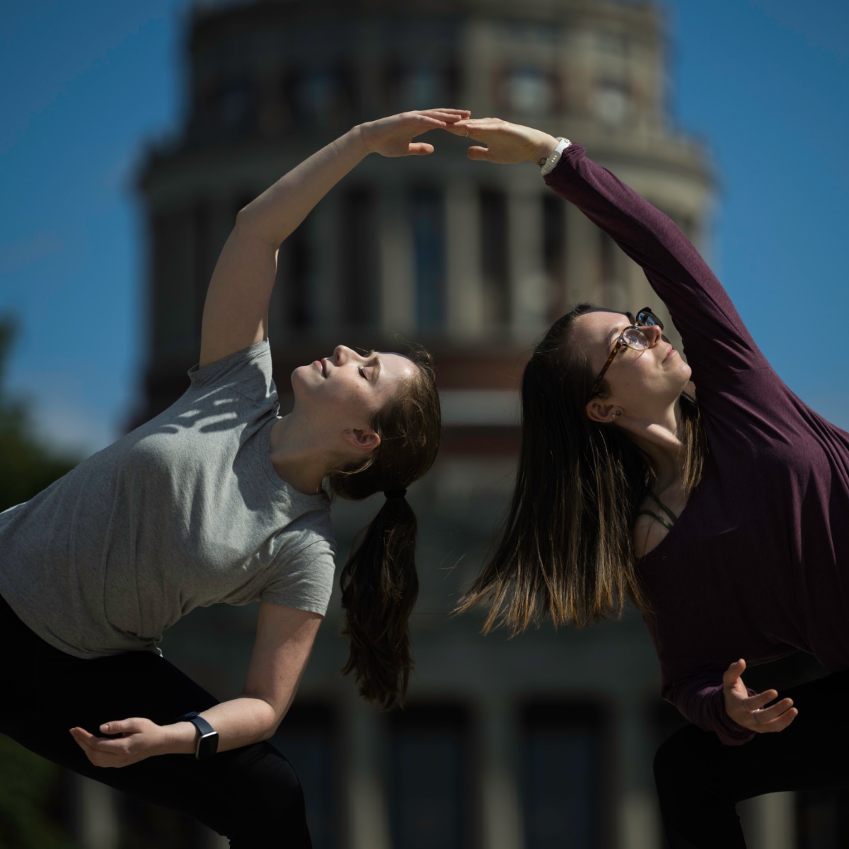 Two students side bend towards each other so their hands meet on the quad