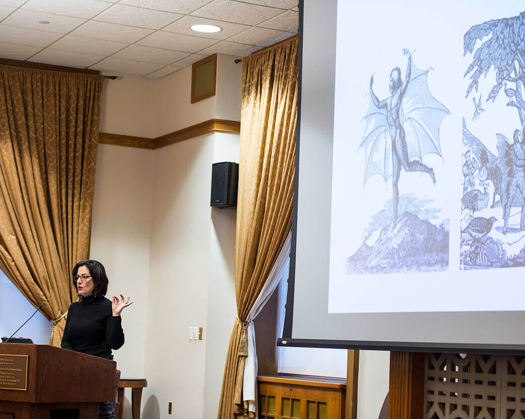 Presenter behind podium in front of projector screen at University of Rochester Humanities Center