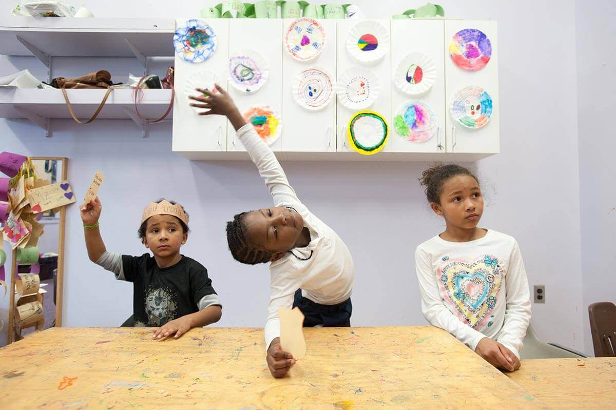 Elementary students at desks raising hands at University of Rochester Mt. Hope Family Center
