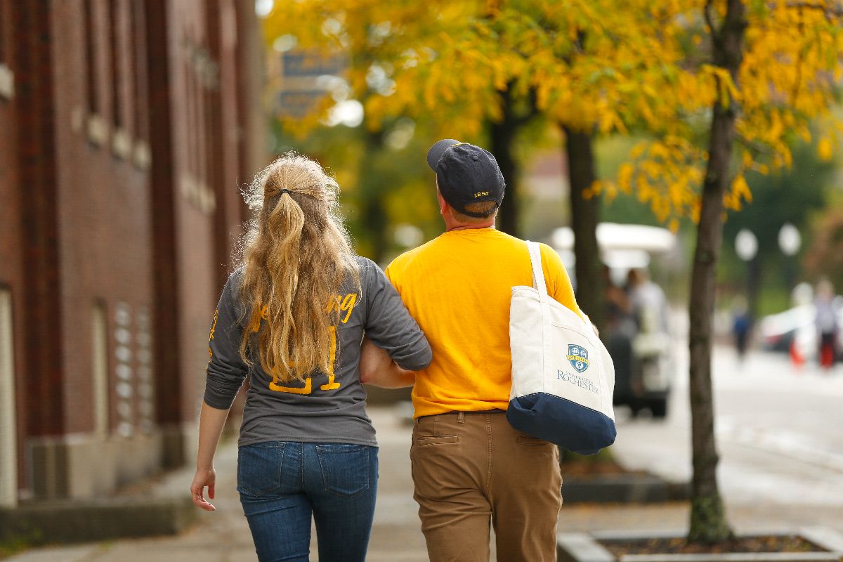 A man and a woman, both URochester students, walking together on a sidewalk.