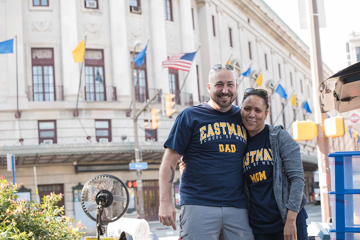 A man and woman pose for a photo in front of the Eastman School of Music at the University of Rochester.