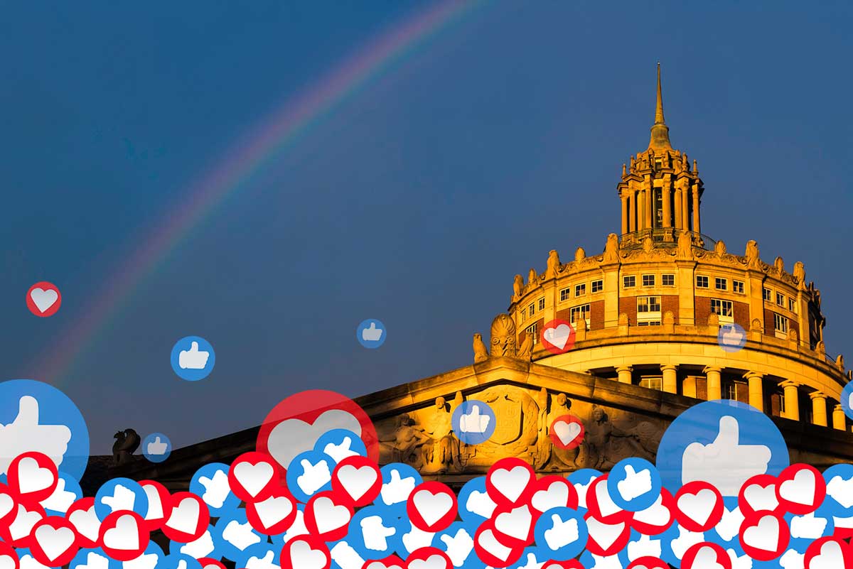 A vibrant rainbow and colorful hearts are displayed in front of the University of Rochester building.