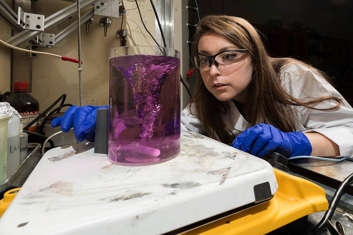 Student researcher looking at beaker of purple liquid in lab at University of Rochester.