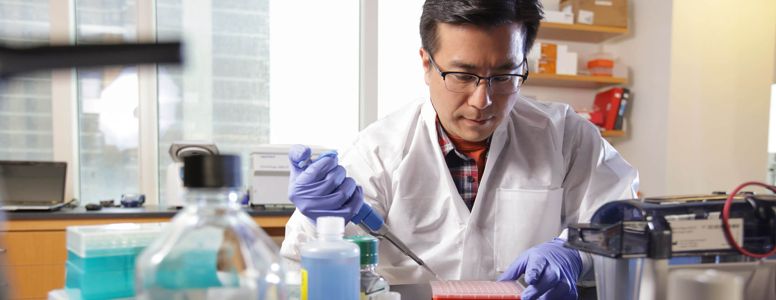 A University of Rochester faculty member in a lab coat works on a project in a laboratory setting.