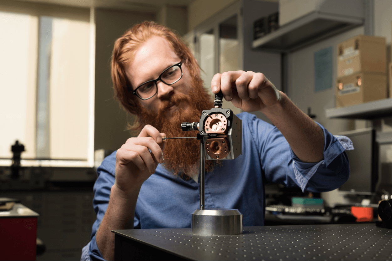 professor looking through an optical instrument on a lab workbench.